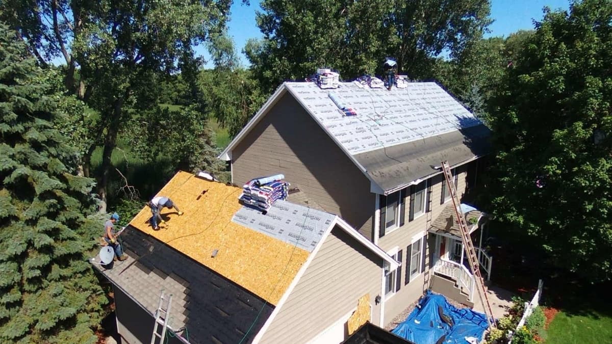 Aerial drone view of active roof replacement with workers installing shingles